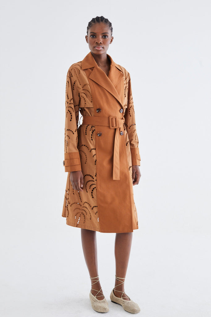 Woman wearing a tan trench coat with a patterned design on a white background