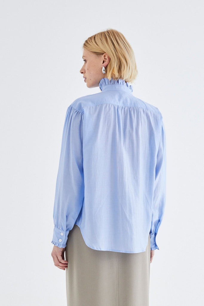 Person wearing a light blue blouse and beige skirt on a white background