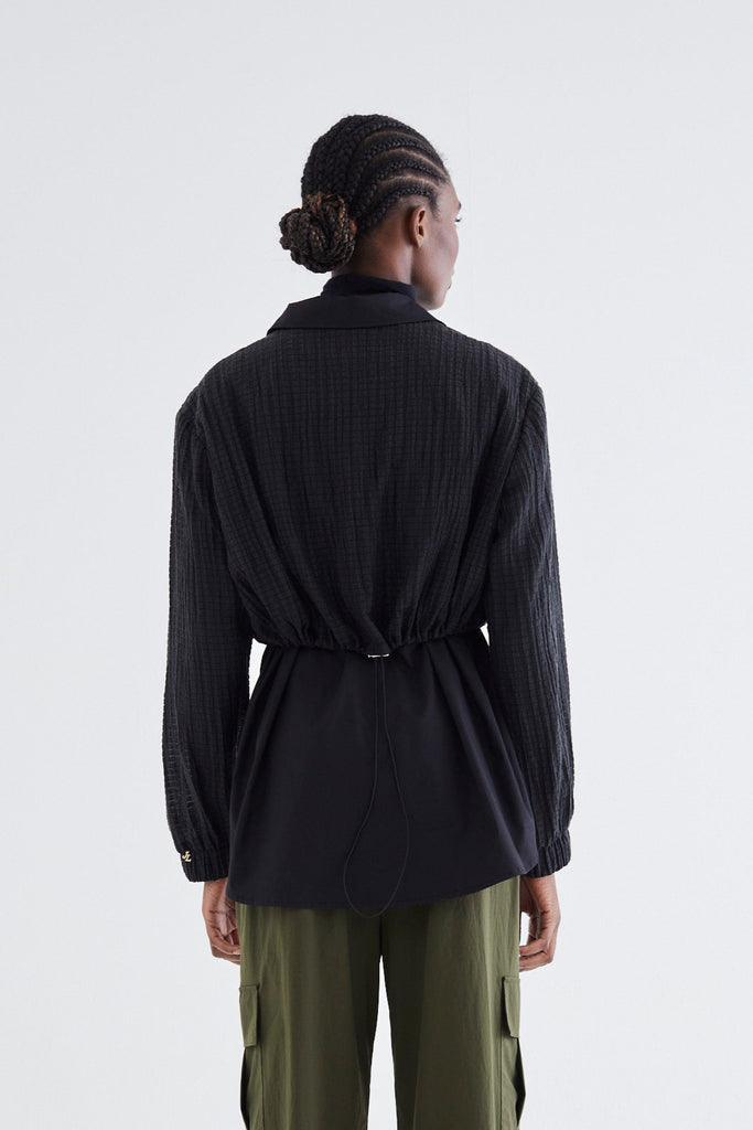 Person wearing a black jacket and green pants on a white background
