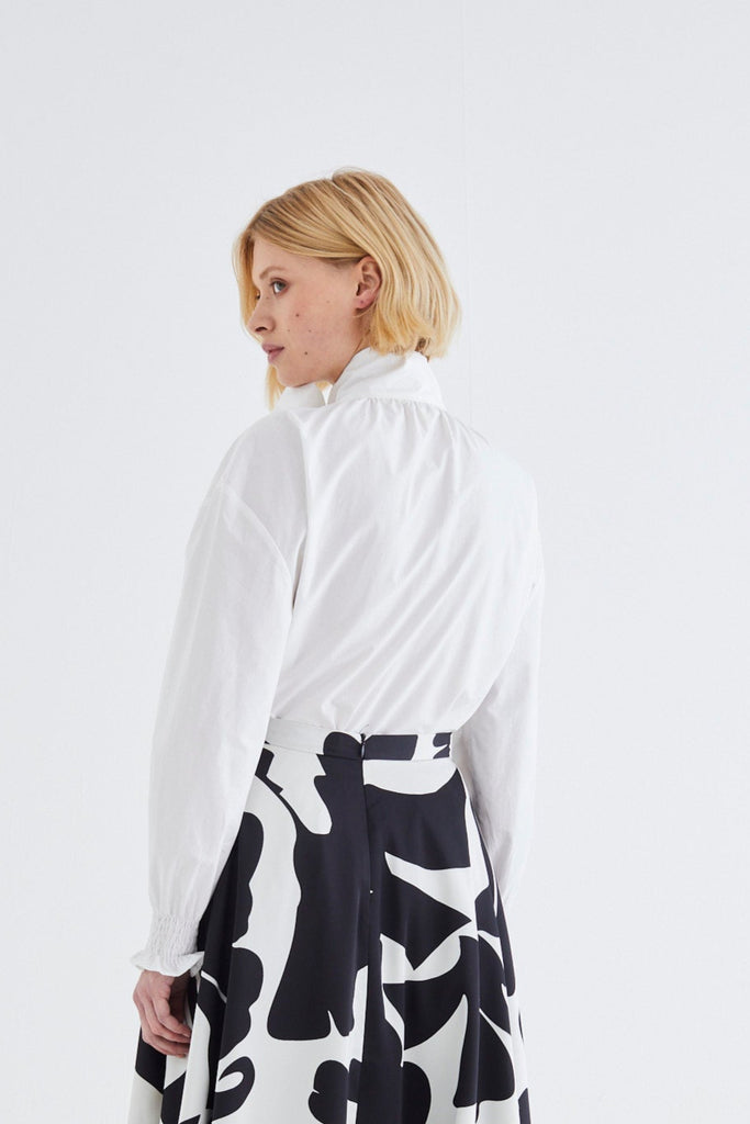 Woman wearing a white blouse and black and white patterned skirt on a white background