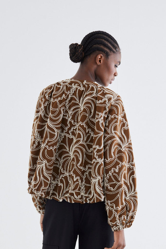 Person wearing a patterned shirt and black pants on a white background