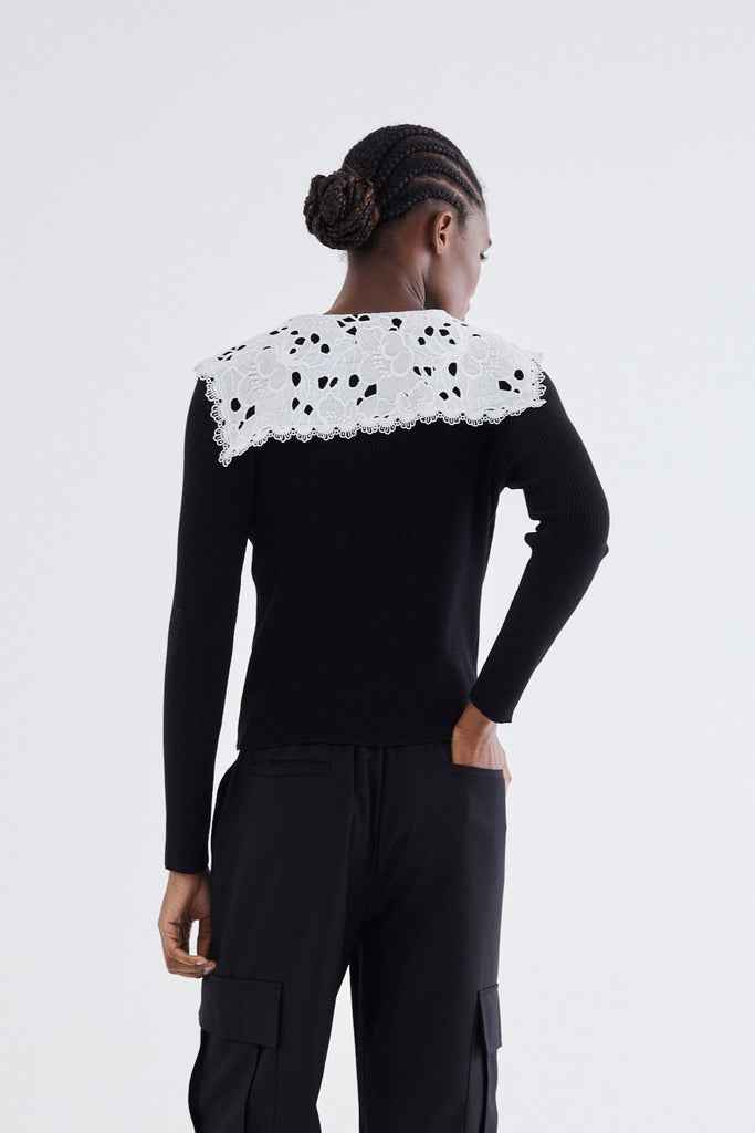 Person wearing a black outfit with white patterned top on a white background
